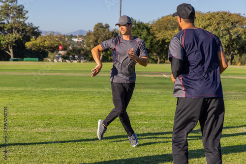 Foto Male teammates throwing red cricket ball while teenage teammate standing ready i