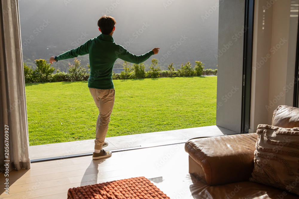 Obraz premium Sliding glass door opening onto sunlit lawn, leather sofa showing textured pillows and orange throw