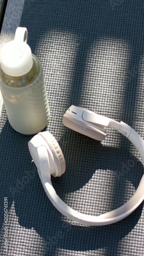 Vertical video: Sunlight shifting, casting slatted shadows on deck mat, lighting headset and bottle