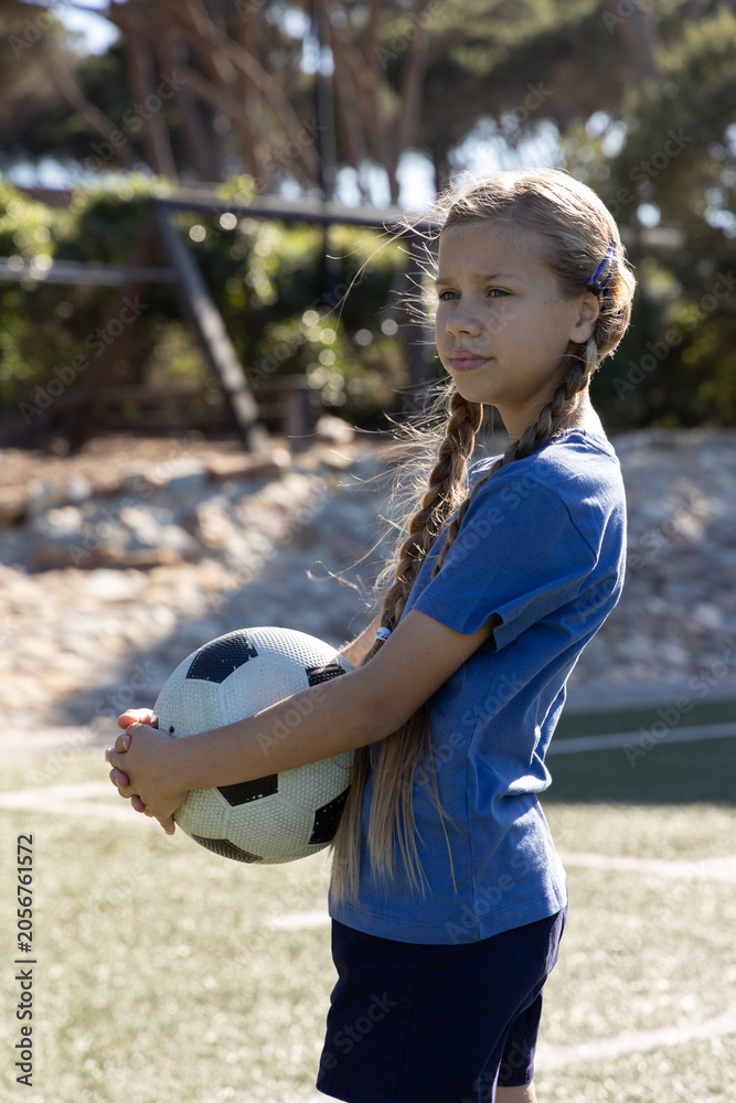 Obraz premium Child girl posing on turf holding black-white soccer ball wearing blue shirt and shorts, copy space