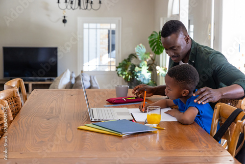 African American father-son father in green shirt working at dining table with laptop, copy space