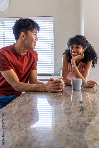 Couple with Asian man holding mug, African American woman in pink top showing smartwatch at counter