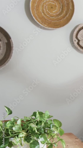Vertical video: Tilting view showing pothos in white pot on wood table to reveal woven baskets