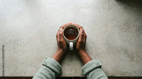 Black Person's Hands Holding Warm Tea Mug on Concrete Surface, Evoking Cozy Calmness