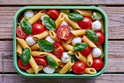 Vibrant pasta salad with mozzarella and fresh tomatoes beside wooden surface