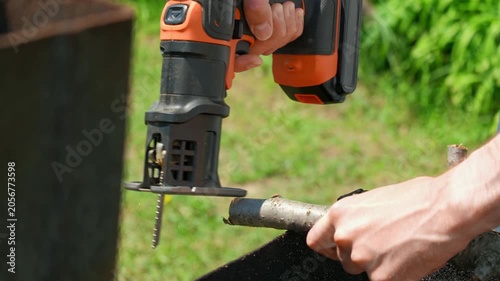 A close-up of a man cutting a branch with a jigsaw