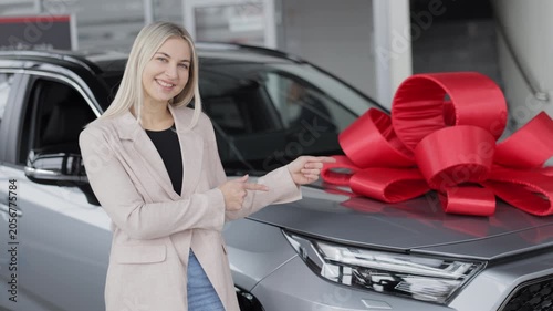 Saleswoman showing new car with red bow in dealership