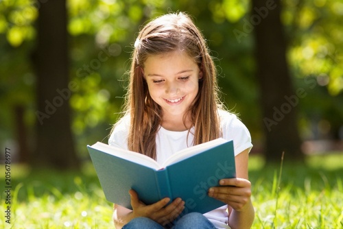 Young girl reading book while sitting on grass in park