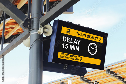 Train delayed information board showing fifteen minute delay at railway station. Passenger notification screen with travel disruption message. Public transport schedule change and waiting time concept