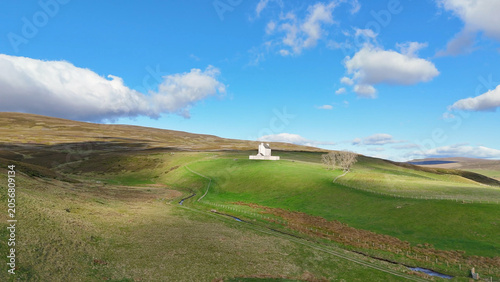 Konstfotografi Corgarff Castle, Scotland, seen from afar across the vast Highland landscape, standing proudly among rolling hills beneath a dramatic sky