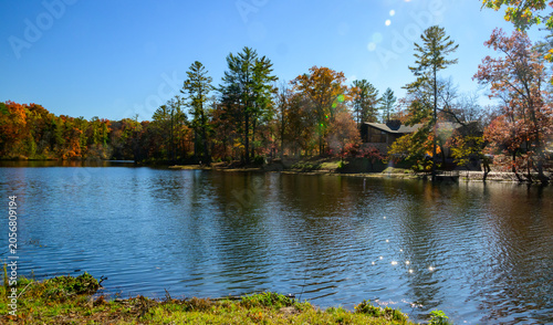 Cumberland Mountain State Park in Crossville, Tennessee, The trees exhibit a vibrant mix of fall colors, including orange, yellow, and red, which are reflected on the water's surface.