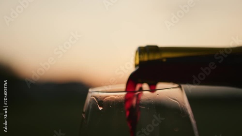 A beautiful sunset sets the scene as rich red wine flows from a bottle into a glass. This moment captures the essence of fine dining and indulgence