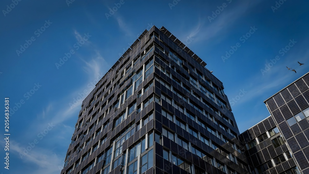 Fototapeta premium Modern tall office building covered in solar panels against a bright blue sky with wispy clouds