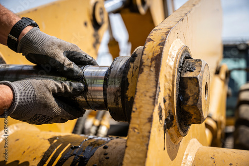 Photography Mechanic wearing gloves inspects greasy heavy machinery pivot point