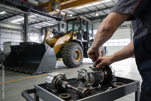 Photos Mechanic working on heavy machinery parts in a workshop with a loader in backgro