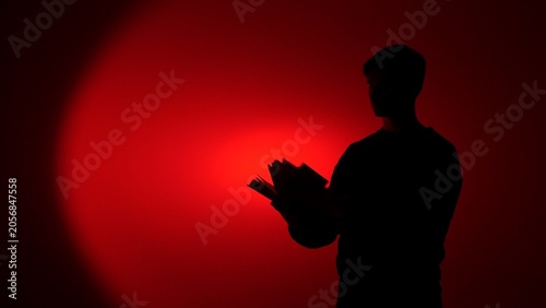 Foto Man's dark silhouette reading book, illuminated by a vibrant red light, creating