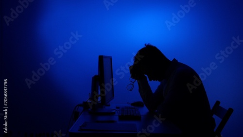 Foto Stressed man leaning head on hands at a desk with a computer, feeling overworked