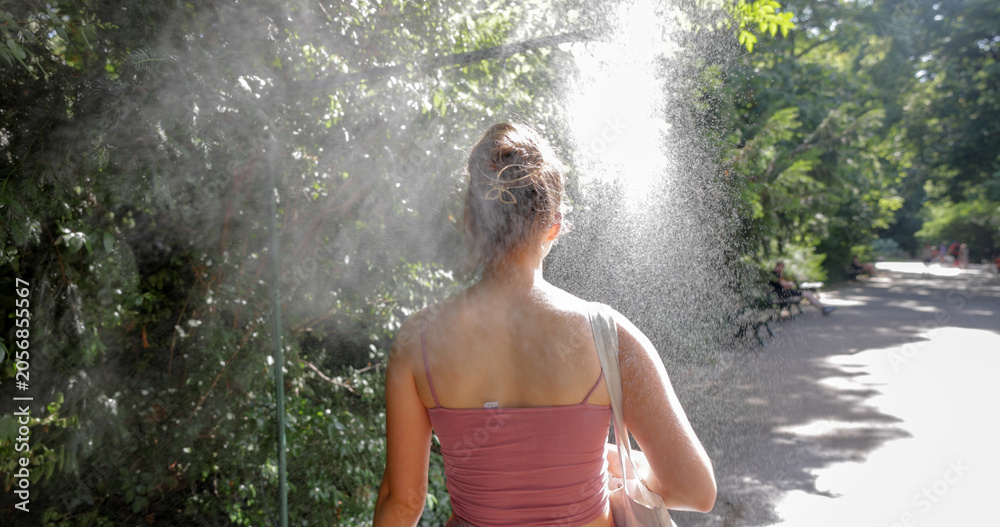 Naklejka premium Young woman cooling down with water mist spray in park