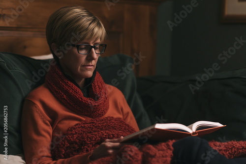 Thoughtful Individual Immersed in a Fictional World While Reading a Thick Novel on a Plush Sofa, Surrounded by Warm Lighting and Inviting Décor