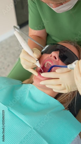 Dentist with Assistant Doing Teeth Cleaning Procedure to Female Patient with Special Tool in Modern Dental Clinic. Caries and Toothache Treatment. Healthcare and Medicine. Slow Motion. Vertical Video