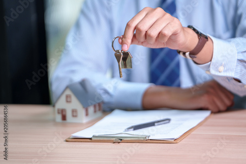 Real estate agent holding house keys above documents on a wooden desk