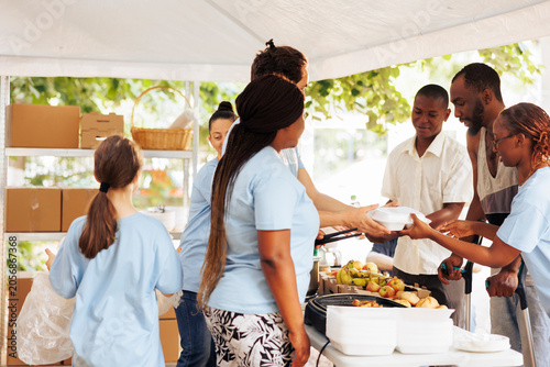 Quadro su tela Woman and multiethnic volunteers helping and giving charitable donations to disadvantaged individuals, with poor, needy and homeless people receive hunger relief support at food drive