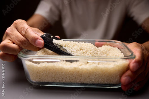 Fotografie Hands digging a smartphone from a container of uncooked rice on a gray surface
