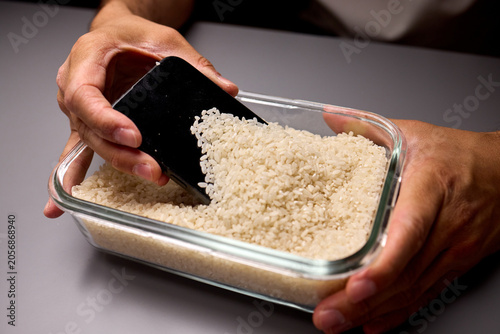 Foto Hands digging a smartphone from a container of uncooked rice on a gray surface