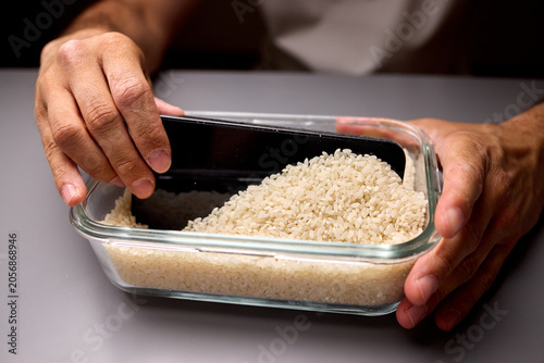 Quadro su tela Hands digging a smartphone from a container of uncooked rice on a gray surface