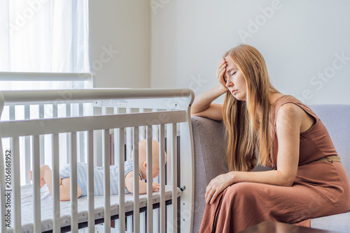 Bilde på lerret Very tired mother sitting by baby crib at home feeling exhausted