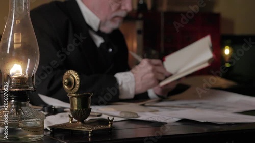 Focus on oil lamp of shipwright writing in a notebook with dip pen