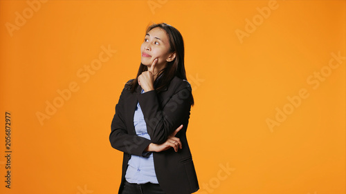 Foto Thoughtful businesswoman posing over orange backdrop, thinking about new ideas and being in doubt, with clueless uncertain person brainstorming solutions, acting focused in front of camera