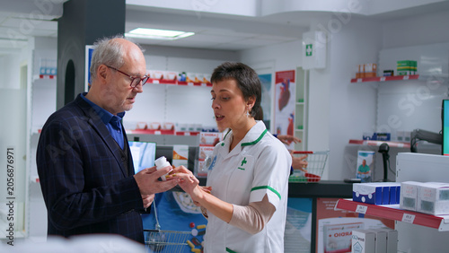 Bild auf Leinwand Knowledgeable pharmacist in pharmacy offering patient heart arrhythmia medication pills to treat disease symptoms, with senior man receiving treatment from helpful drugstore worker