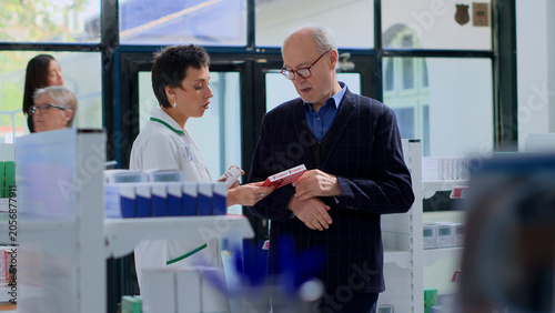 Foto Knowledgeable pharmacist in pharmacy offering older customer antibiotics made for treating disease symptoms, with healthcare specialist in chemist shop helping aged man get rid of heart pain