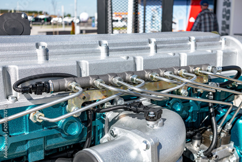 Detailed close-up of an inline marine diesel engine installed in a boat compartment showing turquoise valve covers, metal piping, braided fuel lines, aluminum
