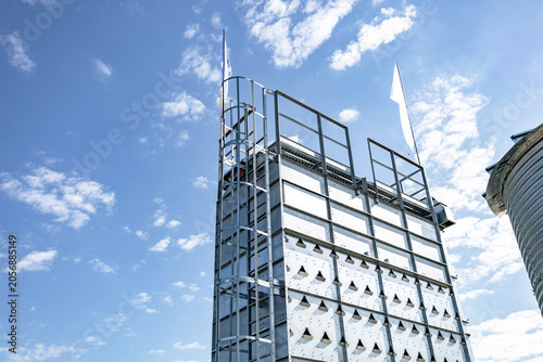 Close-up view of a modern multi-story building facade featuring glass panels and steel framework against a bright blue sky with scattered white clouds