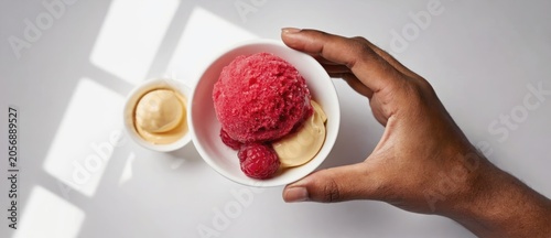 Close up of hand holding ice cream in bowls on a white surface with shadows