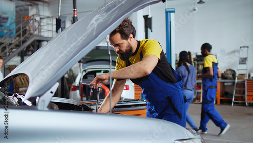 Fotografie Licensed repairman in car service picks torque wrench from work station bench, using IT to tighten bolts after replacing engine