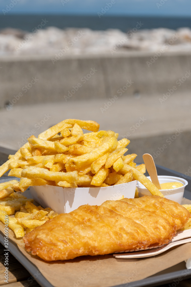 Fototapeta premium Fish and chips on Le Treport promenade golden battered cod with mountain of french fries, seaside flavors enjoyed outdoors by the harbor in Normandy, France