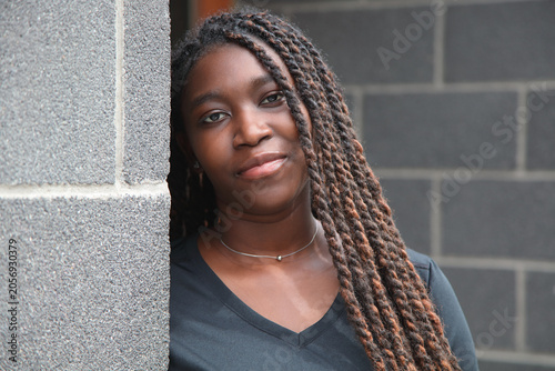 Fotografia Calm young Black woman with long braids leaning against a gray urban concrete wa