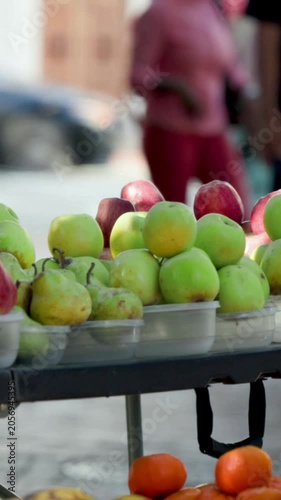 Vertical video: Camera panning, framing fruit stall to keep display centered, people in green pink