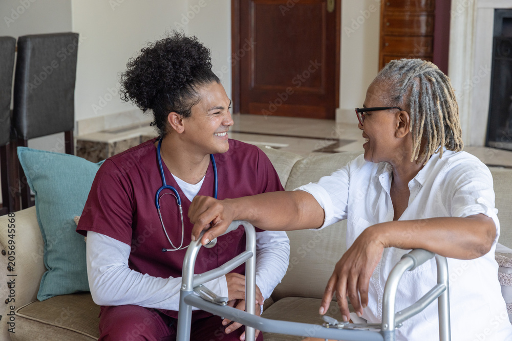 Naklejka premium Male nurse and Senior African-American woman sitting on couch holding walker and stethoscope