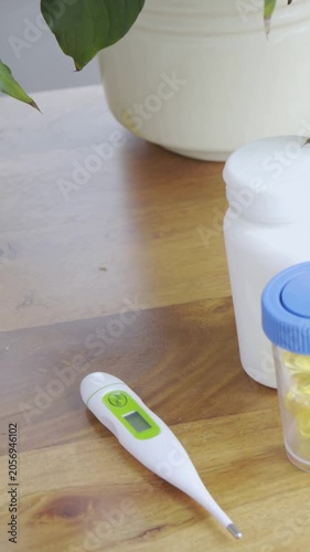 Vertical video: Panning cam revealing thermometer on wood table opening view to plant pot and pills