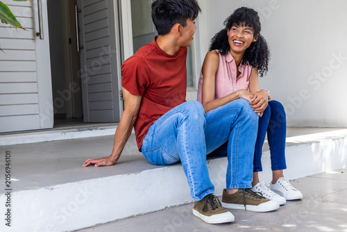 Fotografie Asian man telling story to African American woman while sitting on stoop outside