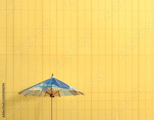A blue and white umbrella stands alone against a vibrant yellow wall with a grid pattern