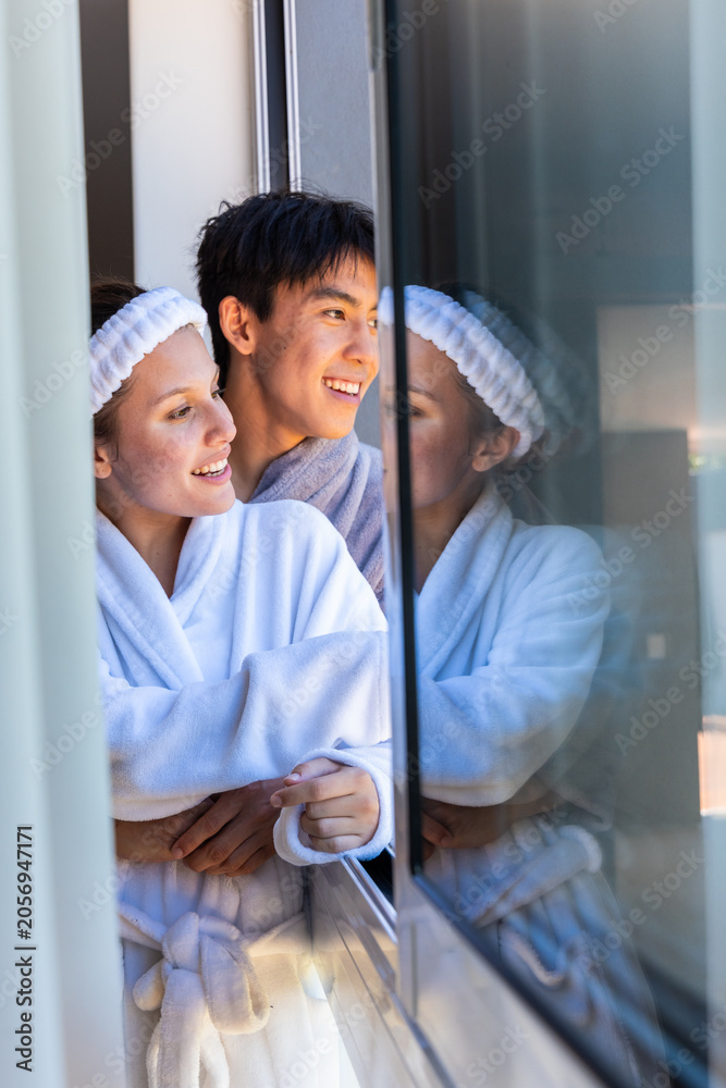 Obraz premium Diverse couple standing at doorway wearing white robes and terry headband reflecting in glass