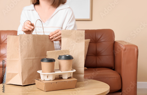 Woman unpacking takeaway food and coffee delivery in brown paper bags and cardboard containers at home, convenience of modern food services and the comfort of enjoying meals at home