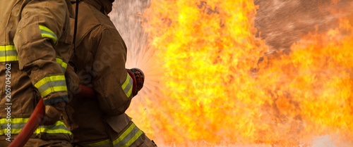 Two firefighters extinguishing a large fire with a hose