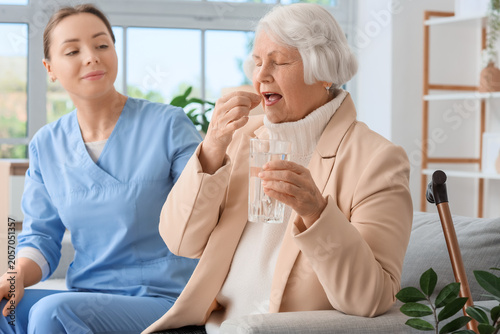 Senior woman with dementia and nurse taking pill on sofa at home