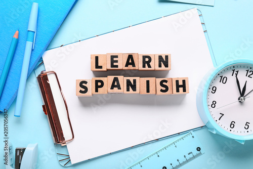 Obraz na płótnie Learn spanish language education with wooden blocks, stationery, and clock on bl
